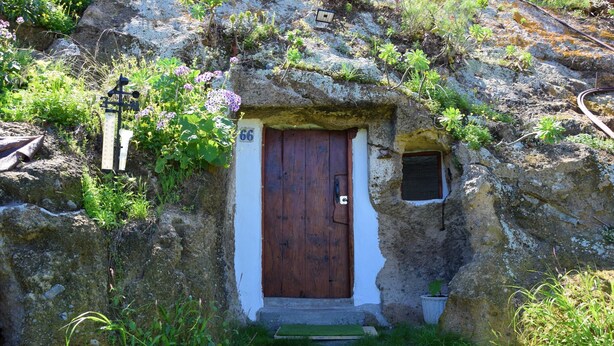 Una casa de piedra rústica con una puerta de madera, una ventana pequeña y el número 66 en la pared.