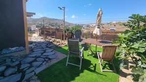 Un patio con una mesa y sillas, un perro acostado sobre una alfombra, y vistas de un pueblo en la ladera.