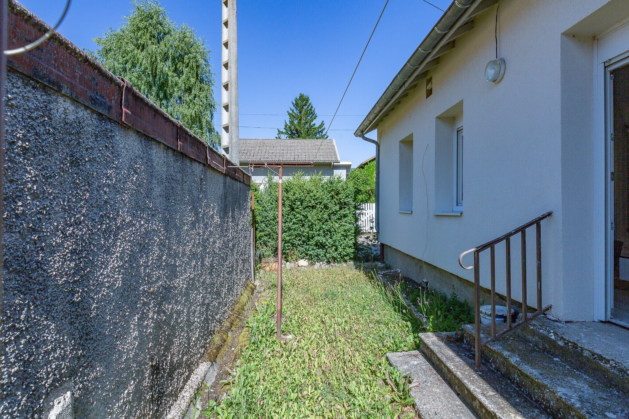Un vicolo stretto con un muro in cemento, una recinzione in metallo e un edificio bianco con una porta e una finestra.