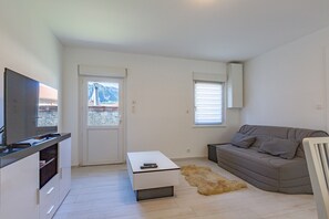 A modern living room with a sofa, a coffee table, a television, and a view of a mountain through a door.