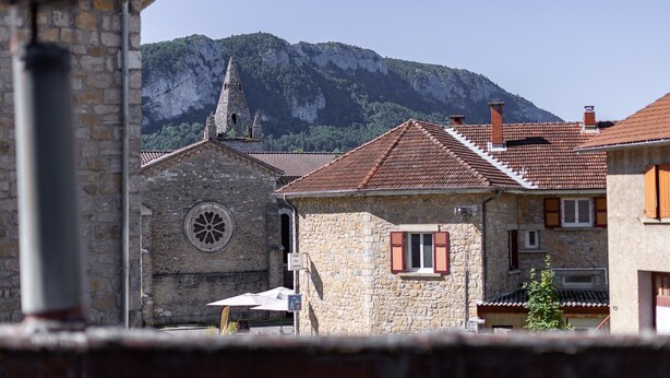 A stone building with a clock tower, red-tiled roofs, and a mountain backdrop.