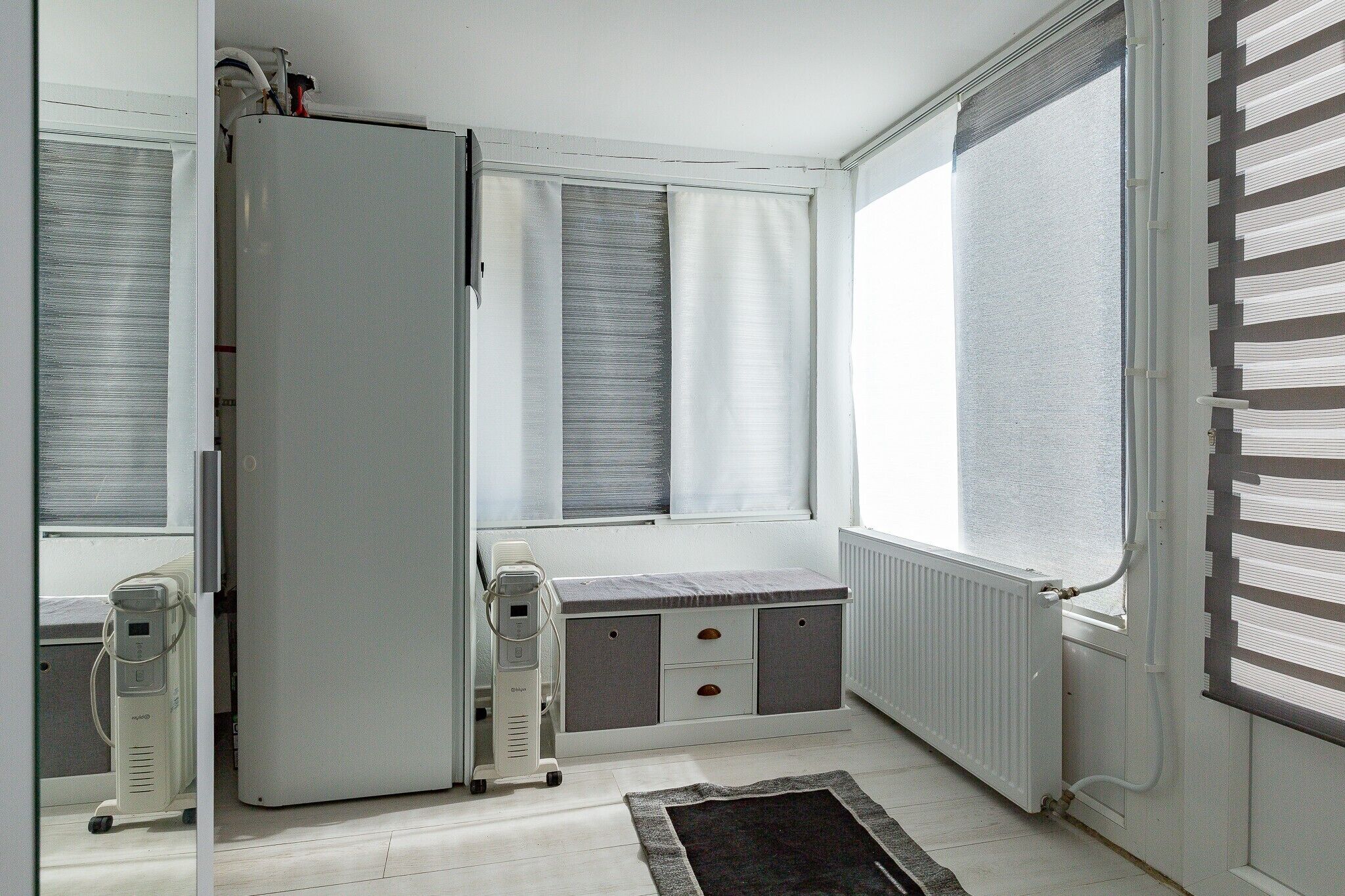 A room with a bed, a radiator, a window with blinds, and a small table.