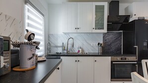 Une cuisine moderne avec des meubles blancs, un pare-feu en marbre, un réfrigérateur noir et un four encastré.