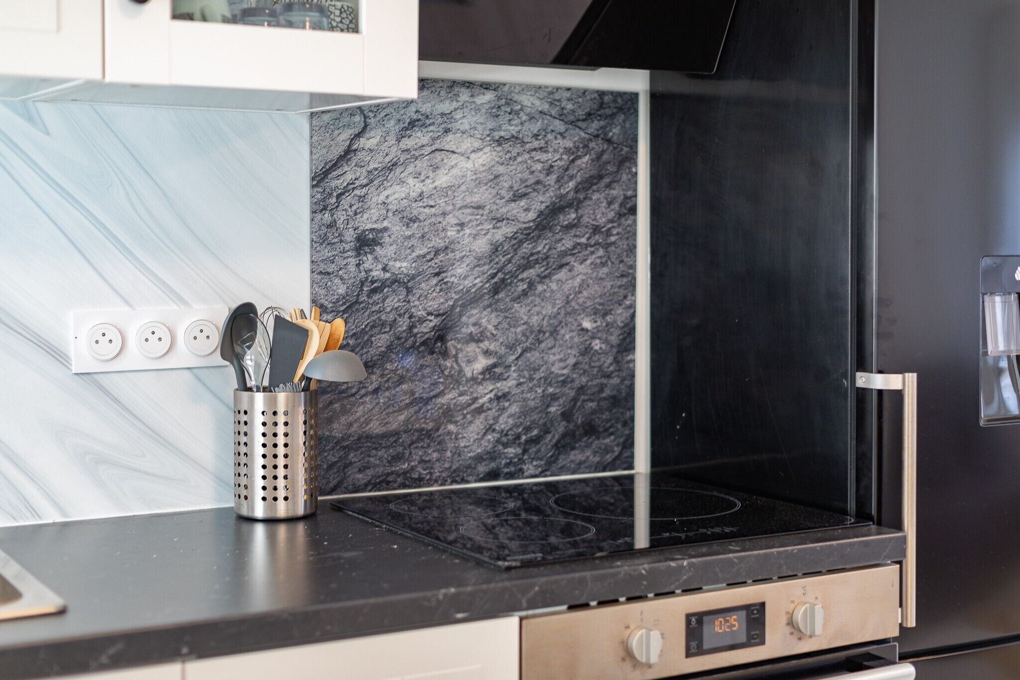 A kitchen with a black stove, a marble backsplash, and a stainless steel oven.