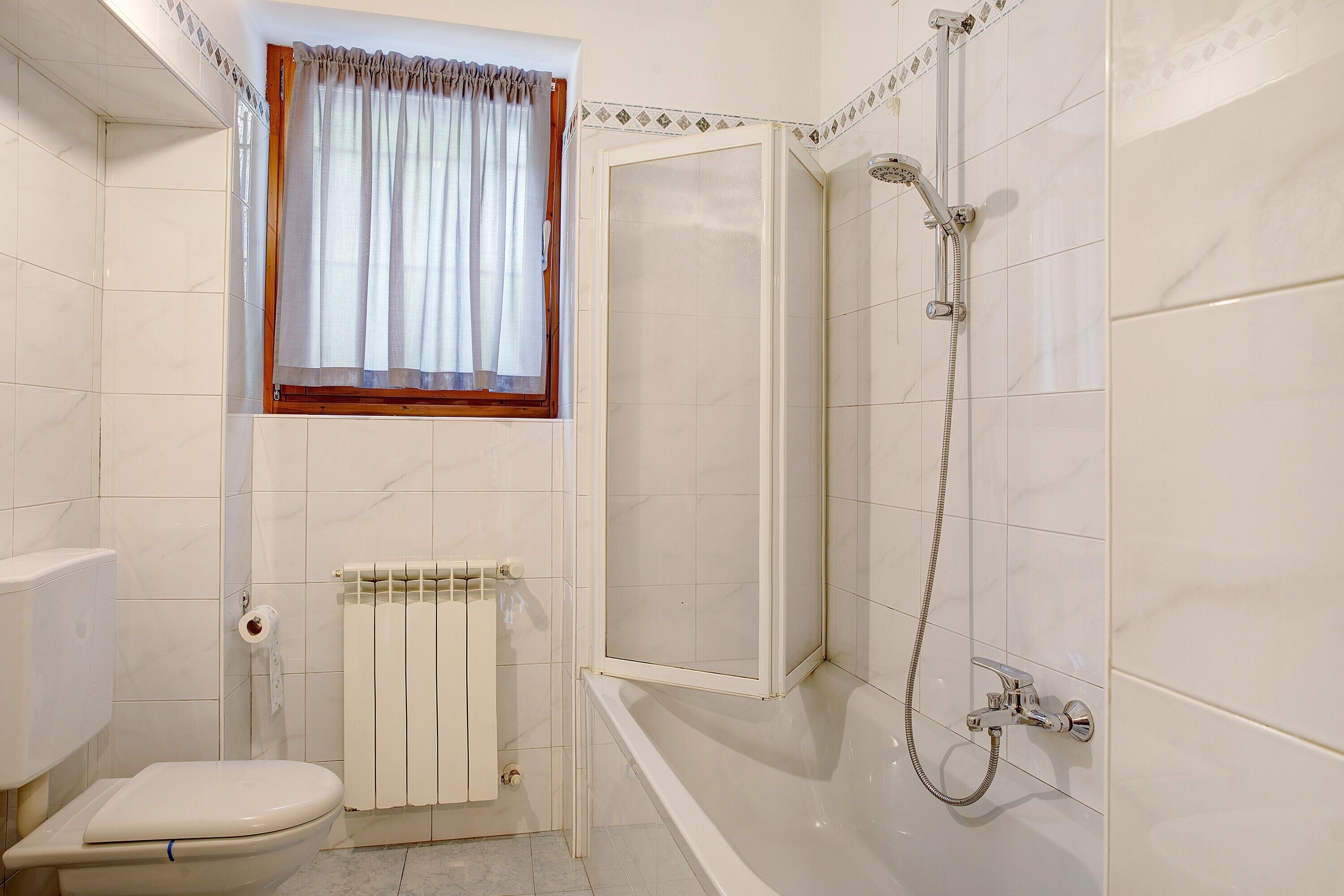 Une salle de bain comprenant des toilettes, une douche, une fenêtre avec des rideaux et un radiateur.