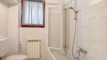 Une salle de bain comprenant des toilettes, une douche, une fenêtre avec des rideaux et un radiateur.