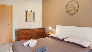 Una camera da letto con un letto, una cassettiera, un comodino con una lampada, un quadro appeso al muro e una porta.