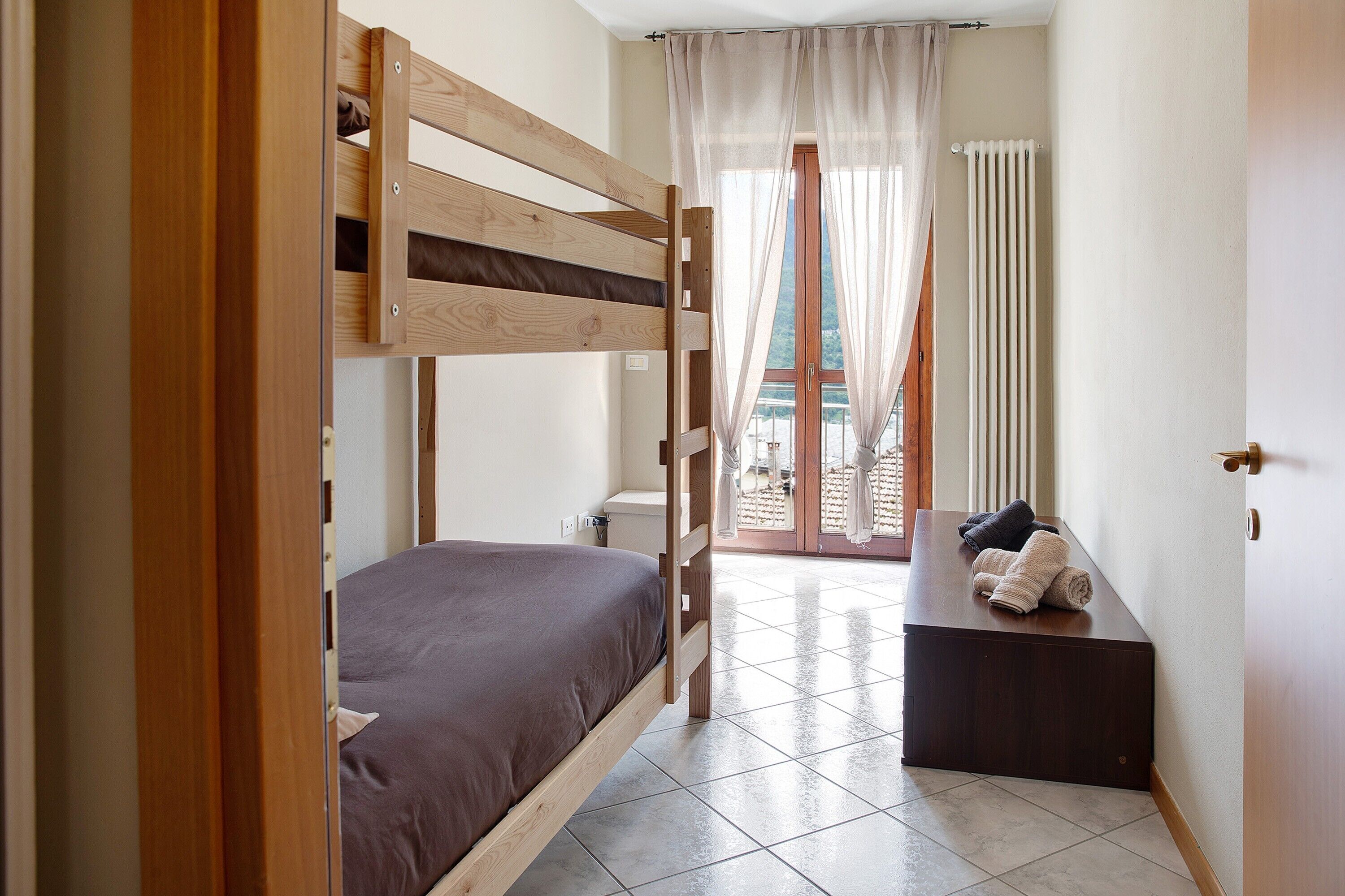 Ein Zimmer mit einem Etagenbett, einem kleinen Schreibtisch, einem Stuhl und einem Fenster mit Vorhängen.