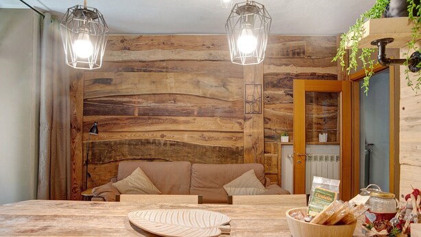 A wooden interior with a sofa, a table with a bowl of bread, and two hanging lights. - Apartment 'Typical  In Valtellina' with Mountain View, Private Terrace and Wi-Fi (Montagna In Valtellina)
