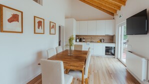 Una cocina moderna con armarios blancos, una mesa de comedor de madera y un televisor montado en la pared.