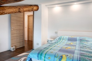 Ein Schlafzimmer mit Holztür, einem Bett mit bunter Bettdecke, einem Nachttisch und einem kleinen weißen Tisch.