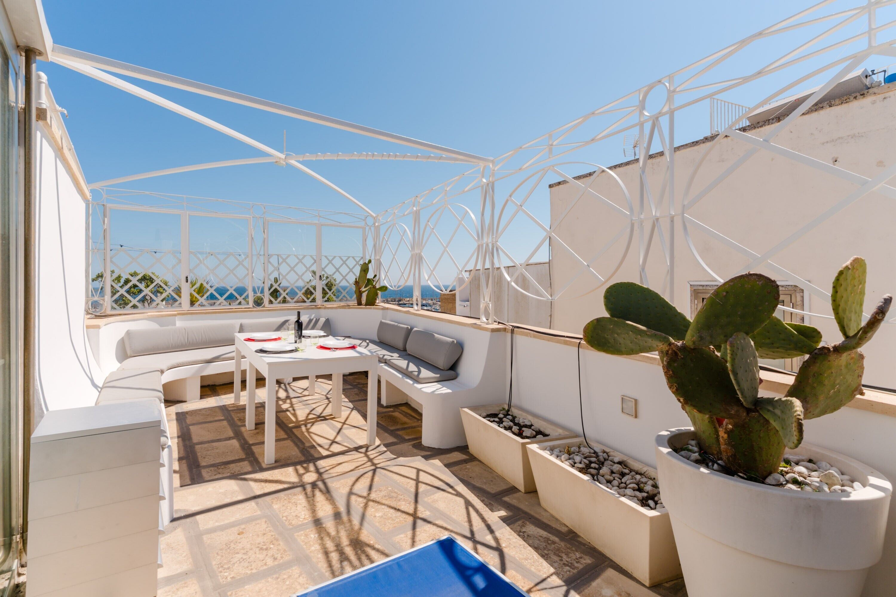 Una terrazza sul tetto con una pergola in metallo bianco, un divano bianco, un tavolino e cactus in vaso.