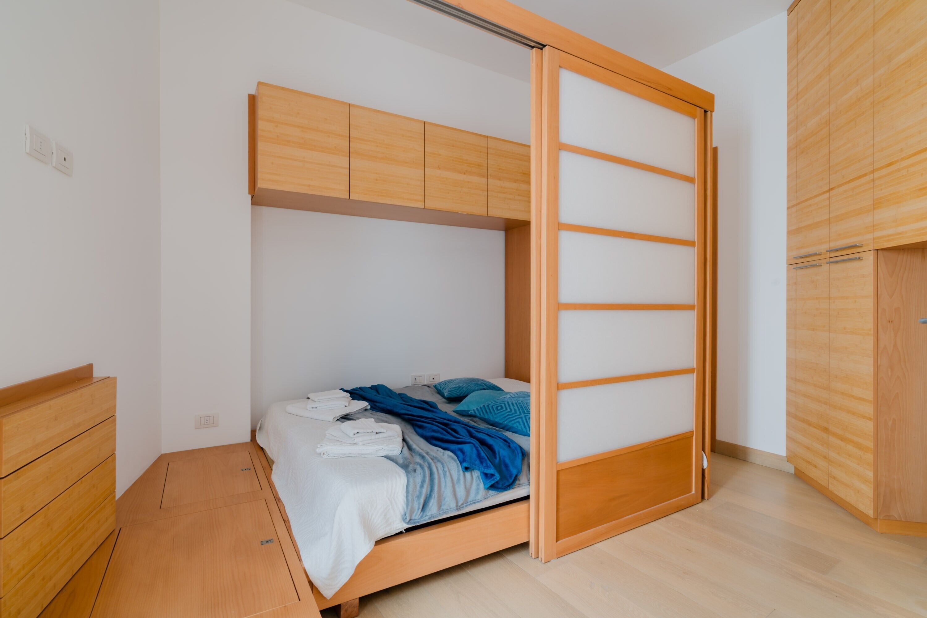 A bedroom with a wooden bed, a sliding door, a wooden wardrobe, and a bedside table.