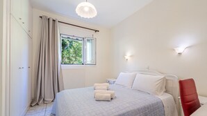 A bedroom with a bed, bedside tables, a window with curtains, and a red chair.