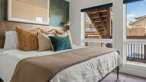 Ein Schlafzimmer mit einem großen Bett, Blick auf eine Holzterrasse und einem gerahmten Kunstwerk an der Wand.