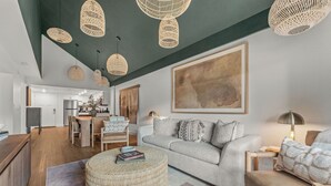 Ein modernes Wohnzimmer mit einem grauen Sofa, einem runden Hocker und Lampen aus Weidengeflecht an der Decke.