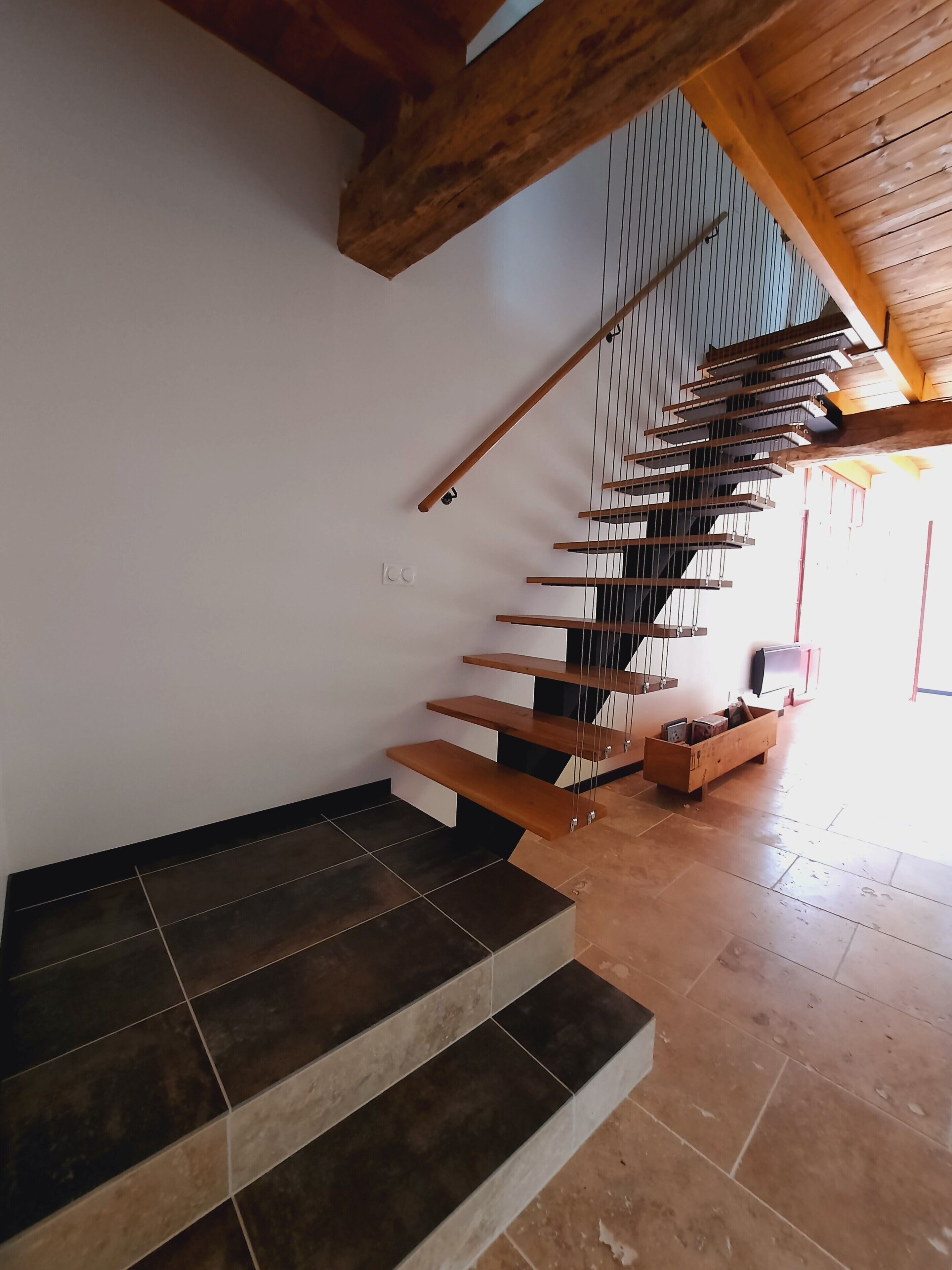 A modern staircase with wooden steps and metal railings, leading to a landing area with a wooden bench and a small table.