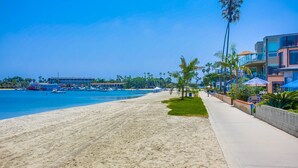 Ein Strand mit einer Betonpromenade, Palmen und einem Gebäude mit Balkonen mit Blick auf das Wasser.