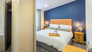 A hotel room with a bed, bedside tables, a nightstand, a wooden desk, and a wardrobe. - Bute Lodge with Hot Tub (Lendalfoot)