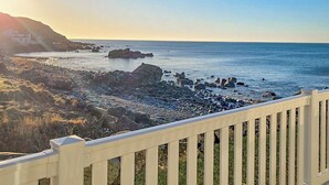 A coastal view with a white fence, rocky shoreline, and a building in the background. - Bute Lodge with Hot Tub (Lendalfoot)