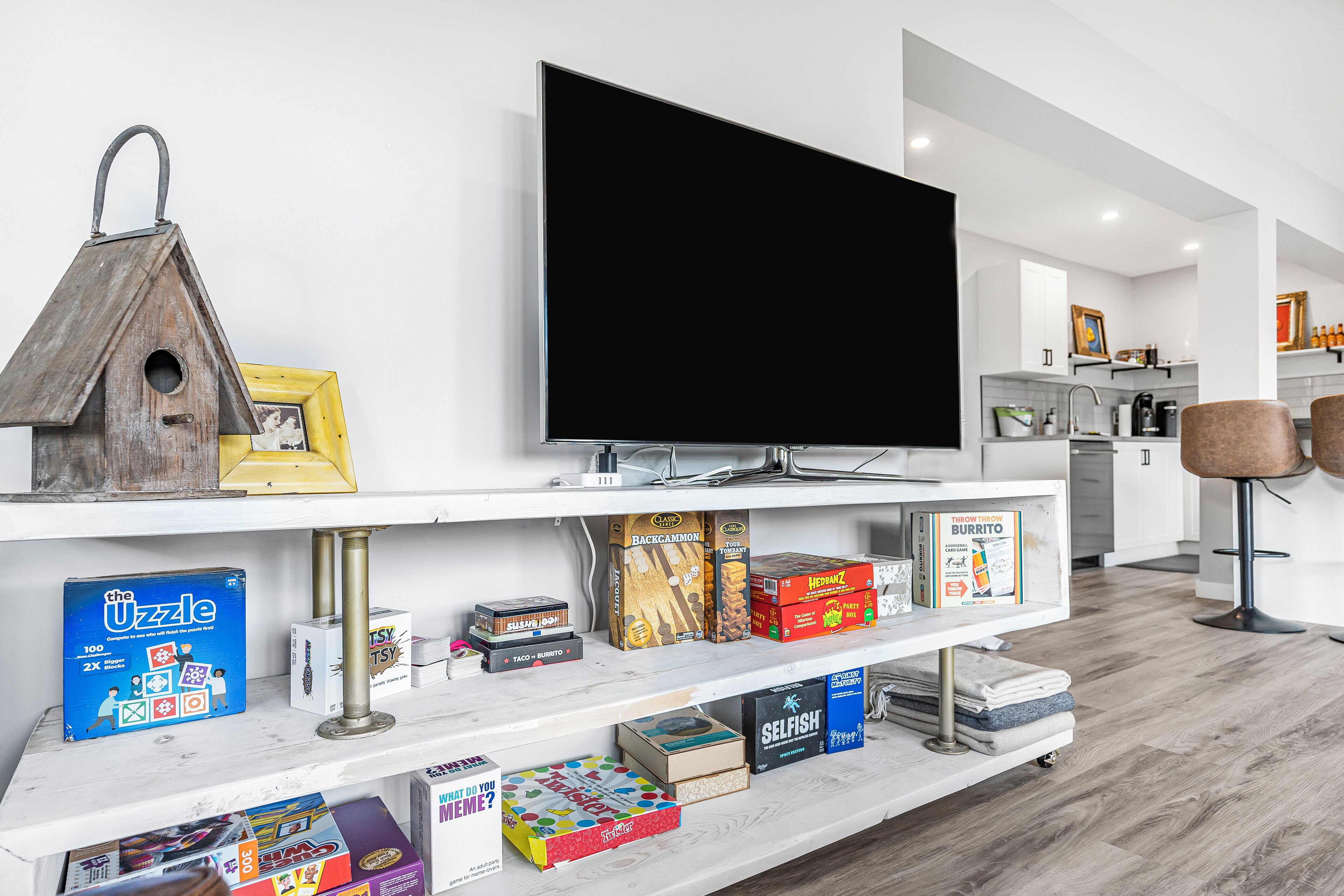 A modern living room with a flat-screen TV, wooden birdhouse, and a variety of board games on shelves.