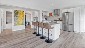 Een moderne keuken met een centraal eiland, barkrukken, roestvrijstalen apparatuur en een groot abstract schilderij.