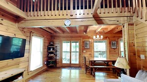 A wooden cabin interior with a TV, dining table, chandelier, and a bookshelf. - Gatlinburg Resort Cabin - Hot Tub, Game Room, Sleeps 6  BOOK NOW FOR FALL COLORS (Gatlinburg)