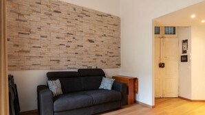 Une pièce avec un canapé foncé, une table d’appoint en bois, un mur au motif de briques et une porte à l’arrière-plan.