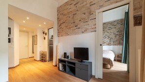 Une chambre moderne avec un mur d’accent en briques, un lit, une télévision et un dressing.