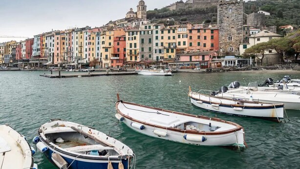 Una costa con edificios coloridos, un castillo y barcos amarrados.