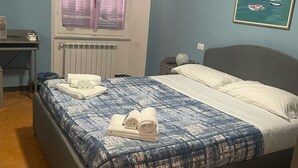 Un dormitorio con cama, escritorio, radiador, ventana con cortinas y un cuadro en la pared.