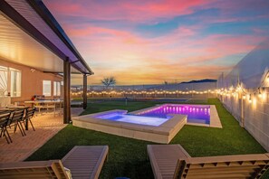 Un jardin avec une piscine, un espace salon extérieur et des guirlandes lumineuses.