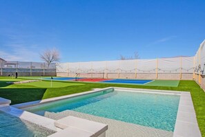 Une piscine entourée d’une terrasse, un court de tennis et un espace couvert protégé par un filet.