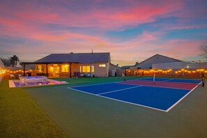 Un court de tennis avec une piscine, une maison et des guirlandes lumineuses.