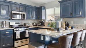 A modern kitchen with dark blue cabinets, stainless steel appliances, granite countertops, and bar stools. - Fun house with Games! (North Las Vegas)