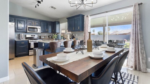 A modern kitchen with dark blue cabinets, stainless steel appliances, and a dining area with a wooden table and chairs. - Fun house with Games! (North Las Vegas)