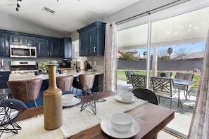 A modern kitchen with dark blue cabinets, a dining area with a table and chairs, and a view of a backyard with a patio.
