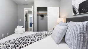 A hotel room with a bed, a bedside table with a lamp, a wardrobe, and a hallway leading to another room. - Fun house with Games! (North Las Vegas)
