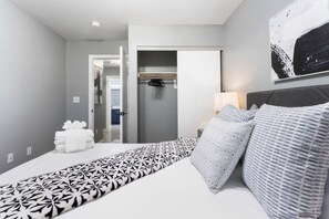 Una habitación de hotel con una cama, una mesita de noche con lámpara, un armario y un pasillo que conduce a otra habitación.