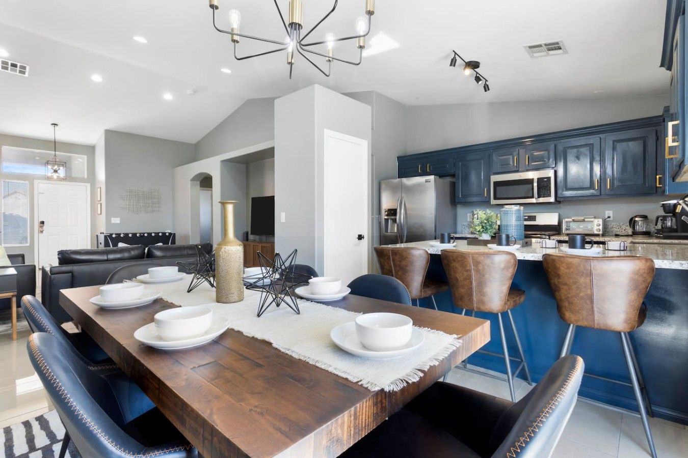 A modern kitchen with dark blue cabinets, stainless steel appliances, and a wooden dining table set for six.