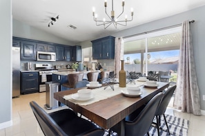A modern kitchen with dark blue cabinets, stainless steel appliances, and a dining area with a wooden table and black chairs.