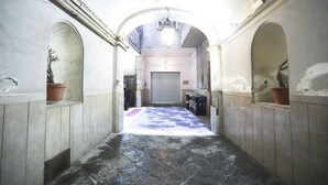 Um corredor com tetos em arco, piso ladrilhado e uma porta central que dá para um quarto com uma persiana fechada.