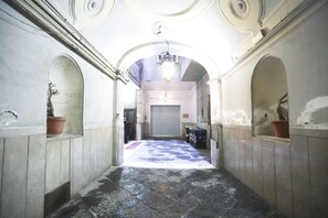 Een gang met gewelfde plafonds, een betegelde vloer, en een centrale deur die leidt naar een kamer met een gesloten luik.