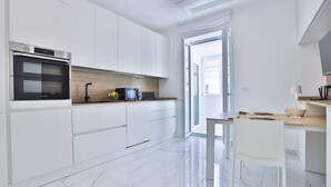 Uma cozinha moderna com armários brancos, forno embutido, bancada de madeira e área de jantar com mesa e cadeiras.