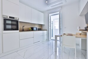 A modern kitchen with white cabinetry, a built-in oven, a wooden countertop, and a dining area with a table and chairs.
