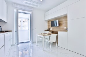 Een moderne keuken met witte kasten, een houten accentmuur, een flatscreen televisie en een eethoek met witte stoelen.