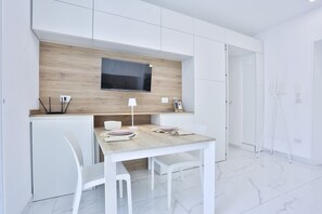 A modern kitchen with white cabinetry, a wooden countertop, a built-in TV, and a dining area with white chairs and a table.