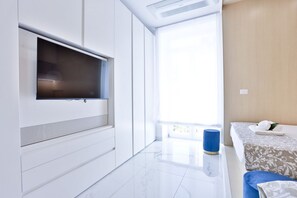 Een moderne hotelkamer met een flatscreen televisie aan een witte muur, een groot raam met uitzicht en een bed met een gestreept dekbed.
