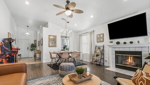 A modern living room with a fireplace, a dining area, and a ceiling fan.