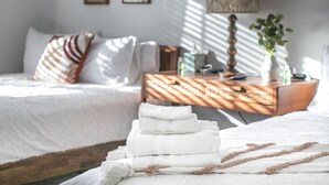 A neatly made bed with folded white towels, a wooden nightstand with a lamp, and a framed picture on the wall.